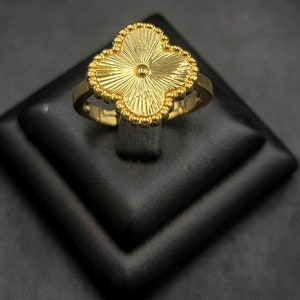 May include: A gold clover-shaped ring with a textured design and a small bead in the centre.