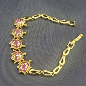 Op de afbeelding: Een gouden armband met een kettingontwerp en vijf schildpadbedels. Elke schildpadbedel is versierd met roze edelstenen.