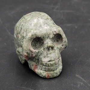 May include: A green and white carved stone skull with red veins. The skull is detailed with eye sockets, a nose, and a mouth.