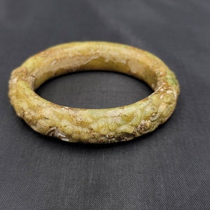 May include: A green jade bangle with intricate carvings. The bangle is smooth and polished, with a light green color.