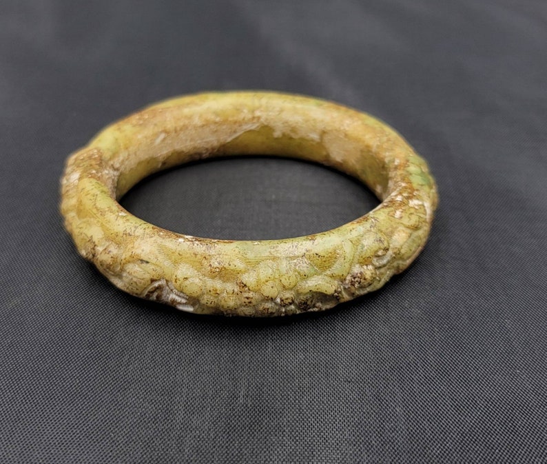 May include: A green jade bangle with intricate carvings. The bangle is smooth and polished, with a light green color.
