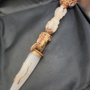 May include: A white quartz dagger with a gold and turquoise handle. The handle is decorated with a dragon head and a series of beads. The dagger is a ceremonial object.