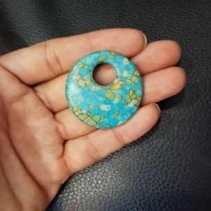 May include: A round turquoise and brown stone pendant with a hole in the center. The stone has a mottled pattern.