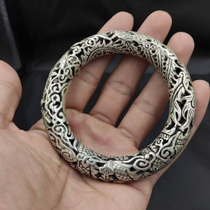 May include: A silver bracelet with an intricate dragon design. The bracelet is open and has a circular shape.