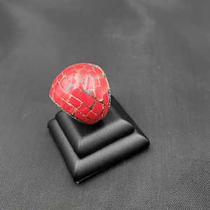 May include: A red mosaic ring with a silver setting. The ring is displayed on a black ring display stand.