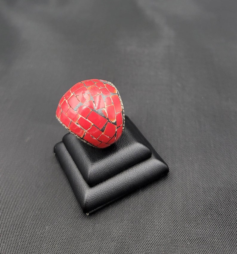 Puede incluir: Un anillo de mosaico rojo con engaste de plata. El anillo se muestra en un expositor de anillos negro.