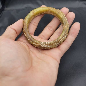 May include: A green jade bangle with intricate carvings. The bangle is smooth and polished, with a light green color.