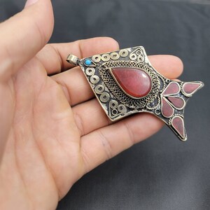 May include: A silver pendant in the shape of a fish with red and turquoise stones. The pendant has intricate filigree details and a red stone in the center.