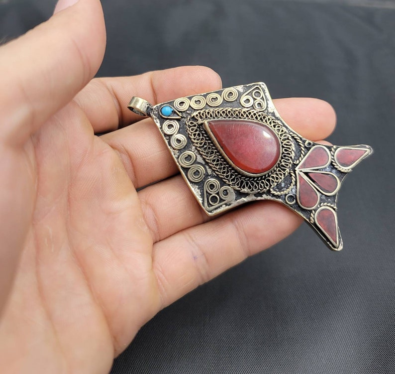 May include: A silver pendant in the shape of a fish with red and turquoise stones. The pendant has intricate filigree details and a red stone in the center.