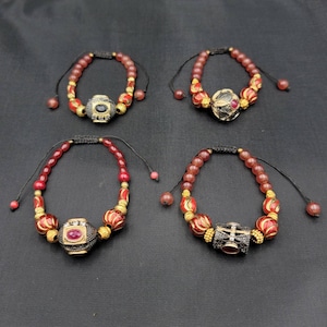 May include: Four red and gold beaded bracelets with decorative charms. Each bracelet features a different charm with a red stone in the center.
