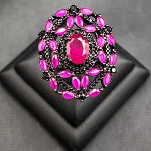 May include: A large, oval-shaped ring with a central pink gemstone surrounded by smaller pink gemstones and black gemstones.
