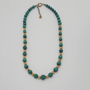 May include: A green malachite bead necklace with gold accents. The necklace is made of round beads and has a clasp closure.
