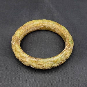 May include: A green jade bangle with a textured surface. The bangle is round and has a smooth, polished finish.