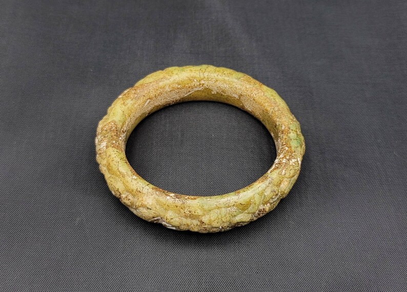 May include: A green jade bangle with a textured surface. The bangle is round and has a smooth, polished finish.