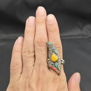 Könnte beinhalten: Ein silberfarbener Ring mit aufwendigem Design. Er hat einen tropfenförmigen gelben Stein, türkisfarbene Akzente und orangefarbene Steine. Der Ring wird an einer Hand getragen.