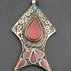 May include: A silver pendant with a red carnelian stone and a turquoise accent. The pendant is decorated with intricate wirework and has a fish-like shape.