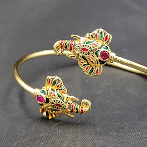 Peut inclure: Un bracelet jonc en or avec deux têtes d'éléphant à chaque extrémité. Les éléphants sont décorés d'émail vert, rouge et blanc et ont de petites pierres précieuses rouges pour les yeux.