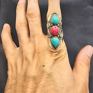 Könnte beinhalten: Ein silberner Ring mit drei Steinen. Die Steine sind türkis und rot. Der Ring befindet sich an einem Finger.