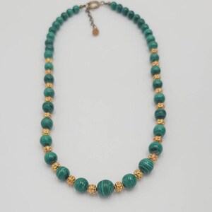 May include: A green malachite bead necklace with gold accents. The necklace is made of round beads and has a clasp closure.
