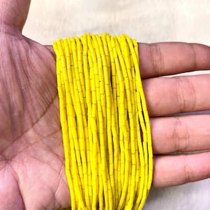 May include: A strand of bright yellow glass beads, each bead is a small cylinder shape. The beads are strung together to form a long strand.