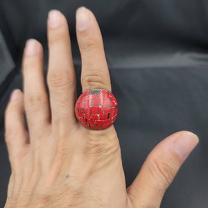 Puede incluir: Un anillo rojo con un dise&ntilde;o de mosaico. El anillo est&aacute; hecho de peque&ntilde;as piezas cuadradas de material rojo.