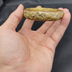 May include: A carved jade bangle with a light green and brown color. The bangle has a floral design.