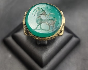 May include: A green gemstone ring with a gold setting. The gemstone features an engraved image of an animal with horns.