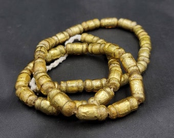 May include: A strand of gold-colored glass beads, with a textured surface, is arranged in a circular shape. The beads are approximately 1 cm in diameter.