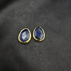 Pode incluir: Um par de brincos de ouro com gotas de pedras preciosas azuis. Os brincos têm a forma de uma lágrima com uma moldura de ouro.