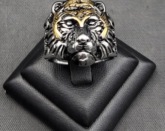 May include: A silver and gold ring featuring a detailed lion head design. The ring is displayed on a black ring display stand.
