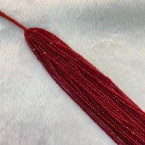 May include: A strand of red faceted gemstone beads. The beads are small and uniform in size, and they are strung on a thin cord.