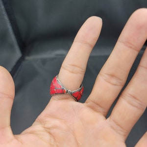 Puede incluir: Un anillo de plata con incrustaciones de piedra roja. El anillo est&aacute; en un dedo.