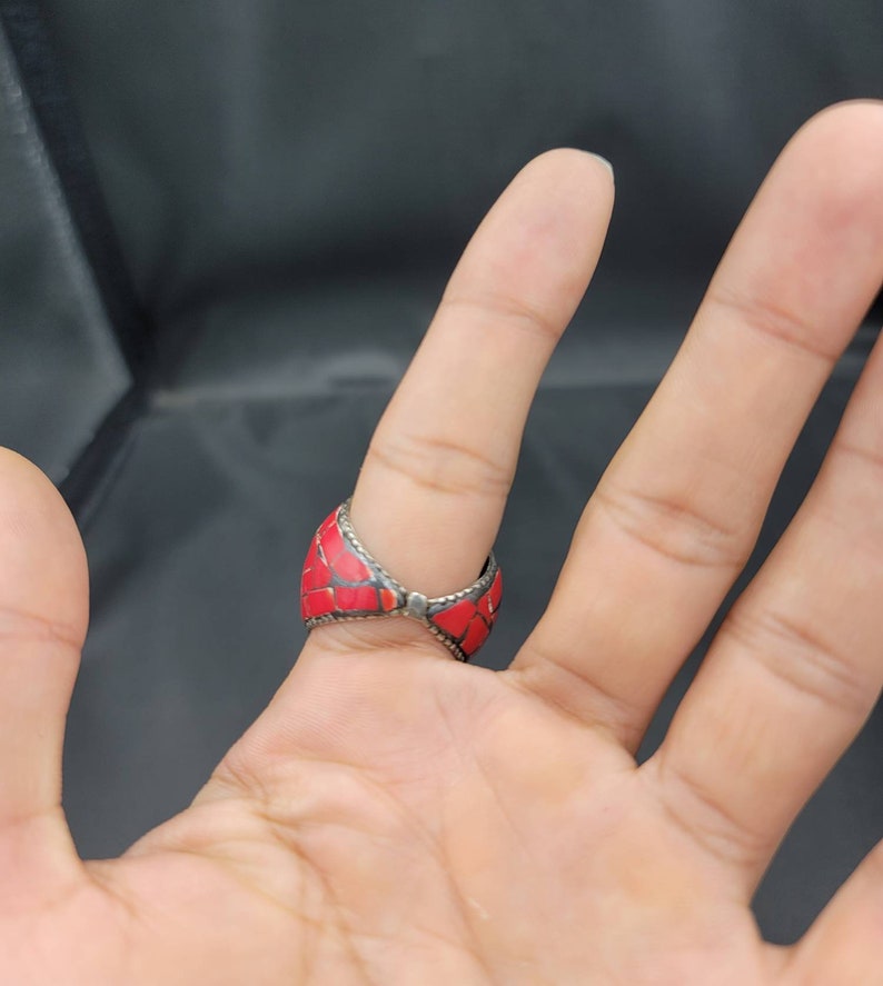 Puede incluir: Un anillo de plata con incrustaciones de piedra roja. El anillo est&aacute; en un dedo.