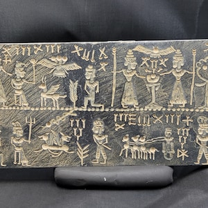 Könnte beinhalten: Eine schwarze Steintafel mit Keilschrift und Bildern von Menschen, Tieren und Pflanzen. Die Tafel ist mit einer Szene einer Prozession von Figuren geschmückt, darunter ein geflügeltes Wesen, eine Ziege und ein Baum. Die Tafel ist ein historisches Artefakt aus dem alten Mesopotamien.