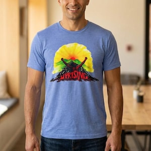 May include: A heathered light blue short-sleeve t-shirt featuring a graphic print of a sun rising over green hills with a dark silhouette of a person with dreadlocks reaching upward and the red text UPRISING printed across the bottom.