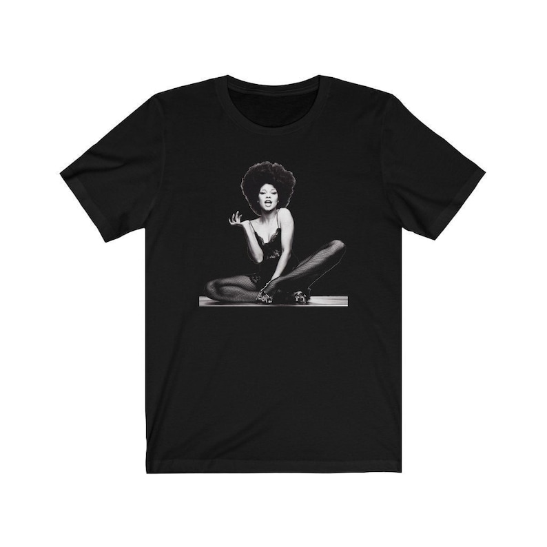 May include: Black and white photo of a woman with an afro sitting with her legs crossed. She is wearing a black leotard and black tights.