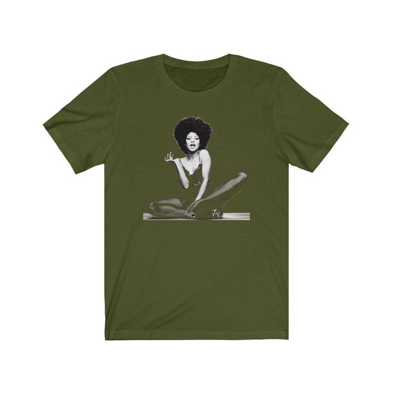 May include: A green t-shirt with a black and white image of a woman with an afro sitting with her legs crossed.