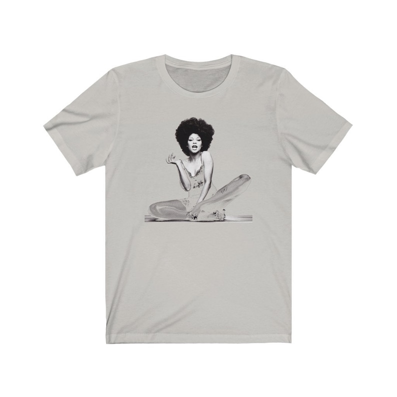 May include: A gray t-shirt with a black and white image of a woman with an afro sitting on a platform.