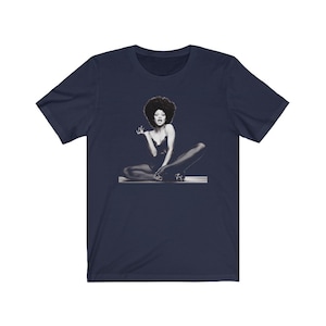 May include: A navy blue t-shirt with a black and white image of a woman with an afro sitting with her legs crossed.