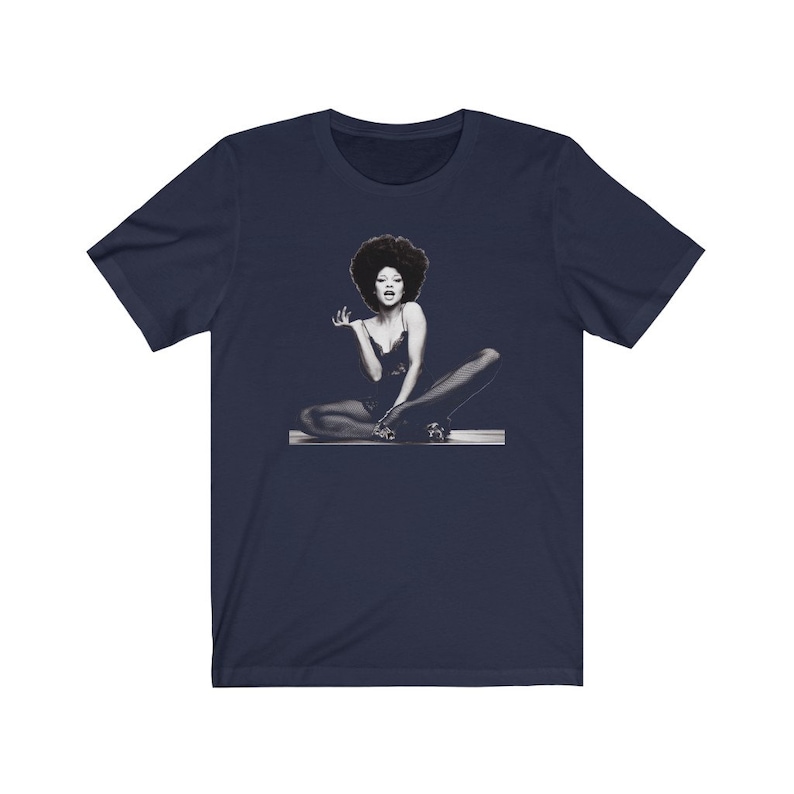 May include: A navy blue t-shirt with a black and white image of a woman with an afro sitting with her legs crossed.