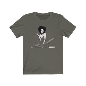 May include: A dark green t-shirt with a black and white image of a woman with an afro sitting with her legs crossed.
