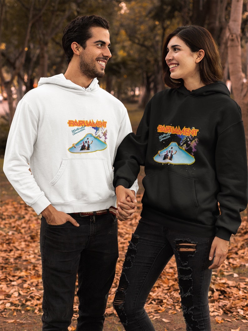 K&ouml;nnte beinhalten: Zwei Personen tragen schwarze und wei&szlig;e Kapuzenpullover mit einer Grafik einer fliegenden Untertasse und dem Text "Parliament Mothership Connection".
