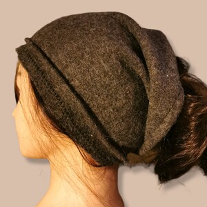 Pode incluir: Um gorro cinza escuro e folgado com uma borda de malha preta. O gorro é feito de um material macio e felpudo.