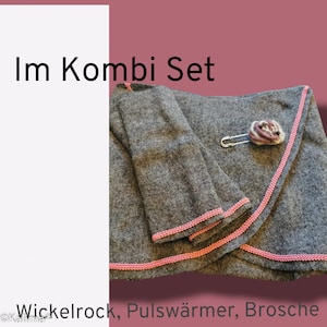 May include: A gray wrap skirt with pink trim, a pair of gray wrist warmers with pink trim, and a gray and purple fabric brooch. The text "Im Kombi Set" is at the top of the image and the text "Wickelrock, Pulswärmer, Brosche" is at the bottom of the image.