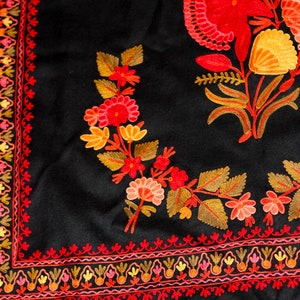 Op de afbeelding: Zwarte sjaal met ingewikkelde borduursels met rode, oranje en gele bloemenmotieven. De sjaal heeft een rand met een herhalend patroon van kleine bloemen en bladeren.