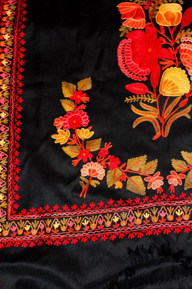 Op de afbeelding: Zwarte sjaal met ingewikkelde borduursels met rode, oranje en gele bloemenmotieven. De sjaal heeft een rand met een herhalend patroon van kleine bloemen en bladeren.