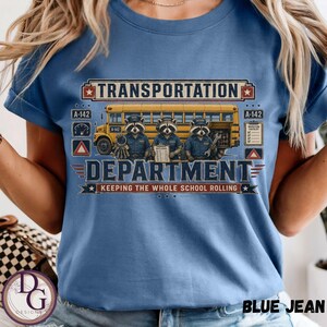 May include: A blue t-shirt featuring a graphic of three raccoons in uniforms standing in front of a yellow school bus. The text reads TRANSPORTATION DEPARTMENT, KEEPING THE WHOLE SCHOOL ROLLING, A-142, and INSPECTION CHECKLIST. The design includes icons of a gauge, a triangle, and stars.