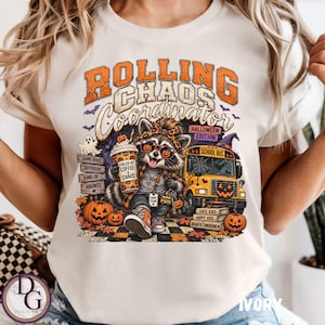 Könnte beinhalten: Ein elfenbeinfarbenes T-Shirt mit einer Grafik eines Waschbären mit Leoparden-Stirnband und Sonnenbrille, der einen Kaffeebecher mit der Aufschrift FUELED BY COFFEE AND CHAOS hält. Text: ROLLING CHAOS COORDINATOR HALLOWEEN EDITION neben einem Schulbus.