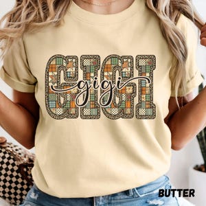 May include: Butter-colored t-shirt with the word "GIGI" in large, patchwork-style letters. The letters are filled with various patterns, including leopard print and plaid. The word "gigi" is written in cursive over the letters.