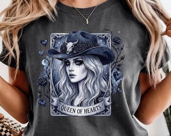 Può includere: T-shirt grigio scuro con un'illustrazione dettagliata di una donna con un cappello da cowboy blu scuro adornato con rose e un teschio. L'immagine è incorniciata con rose e cuori, con la scritta "QUEEN OF HEARTS" su uno stendardo.